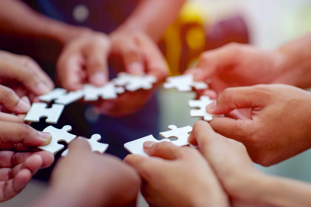 We offer advisory and mentoring services: a ring of people holding puzzle pieces in their hands.