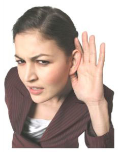 A woman with dark hair and pale skin, wearing a brown jacket and a white inner shirt. She has hearing loss.
