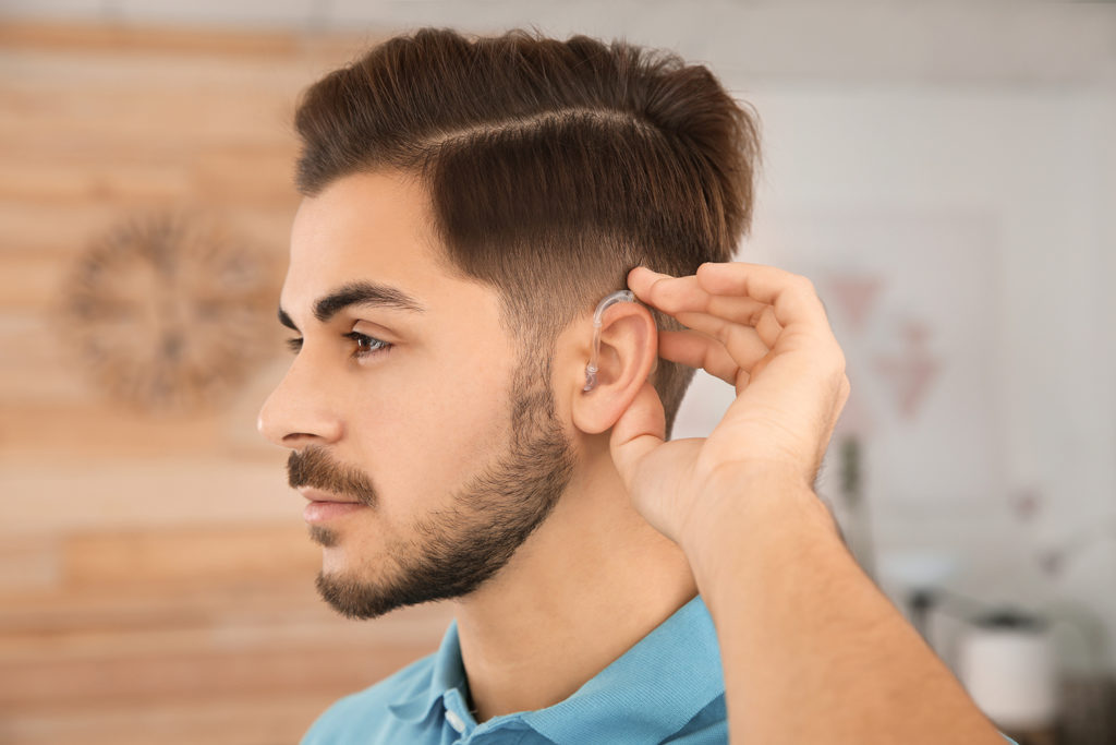 Hear Now! Fund: a young man adjusts his hearing aid. 